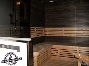 Sauna, jossa tummat seinät ja vaaleat lauteet. Rakennusliike Harju-Heikkilä Oy.
